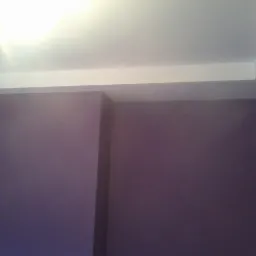 Fioletowa ściana po malowaniu, biały sufit z podwieszanym elementem. Świeżo pomalowane wnętrze z widoczną drabiną w rogu, co sugeruje trwające prace wykończeniowe.