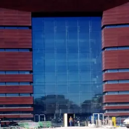 Fasada budynku Narodowego Forum Muzyki we Wrocławiu z konstrukcją szklaną, widoczny pracownik w kamizelce odblaskowej w wejściu.