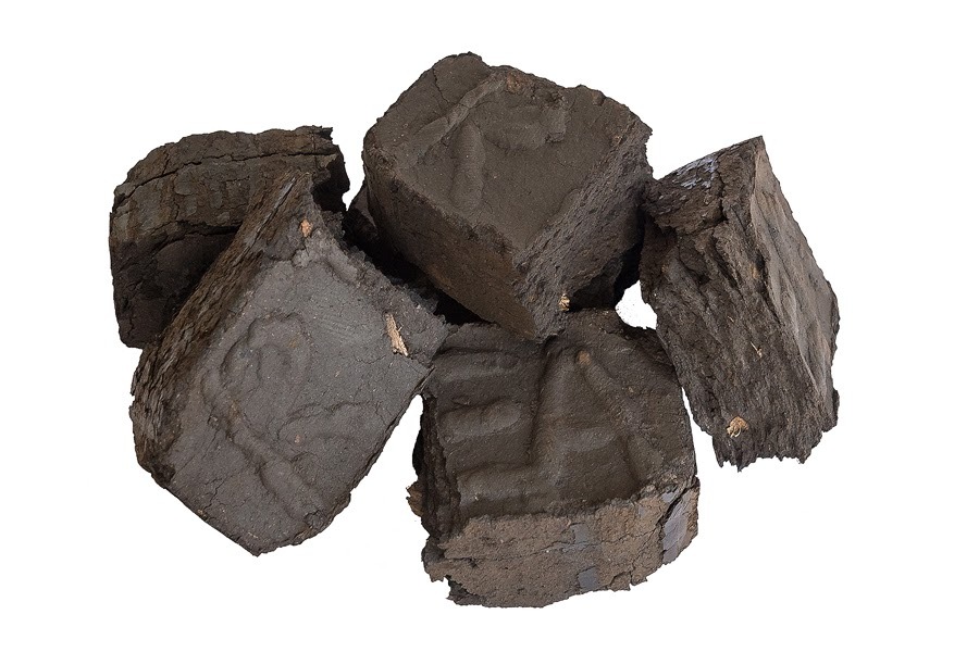 Stos ułożonych kostek ciemnego, prasowanego opału na białym tle, z widocznymi odciskami na niektórych kostkach.