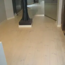 Jasne, odnowione deski podłogowe z widocznym słupem konstrukcyjnym w nowoczesnym wnętrzu.