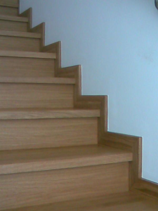 Jasne, drewniane schody z wyraźnym usłojeniem i minimalistycznym wykończeniem, przylegające do białej ściany.