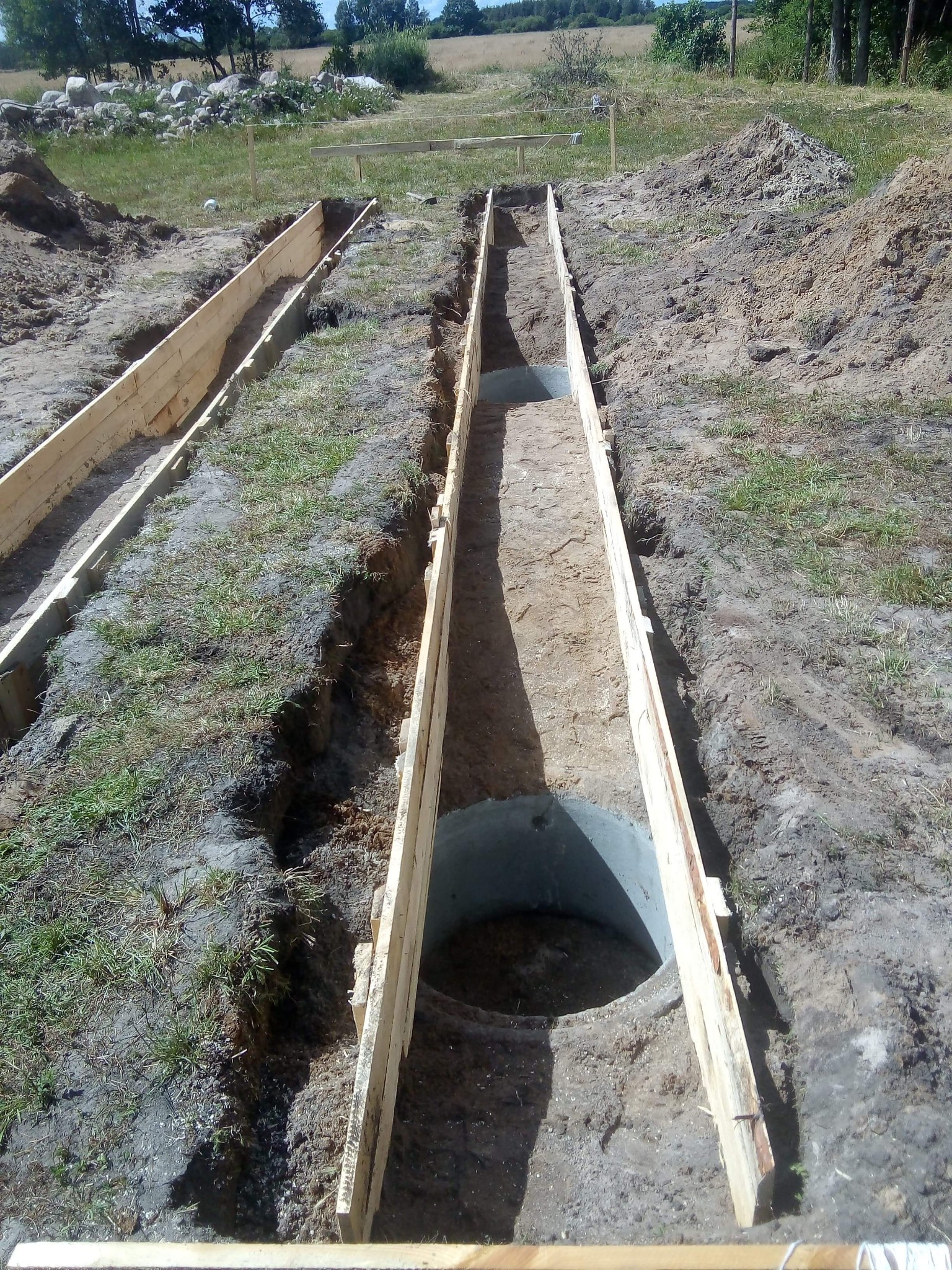 Przygotowanie wykopu pod fundamenty z szalunkiem drewnianym i betonowymi kręgami studziennymi, widok z góry, naturalne oświetlenie dzienne.