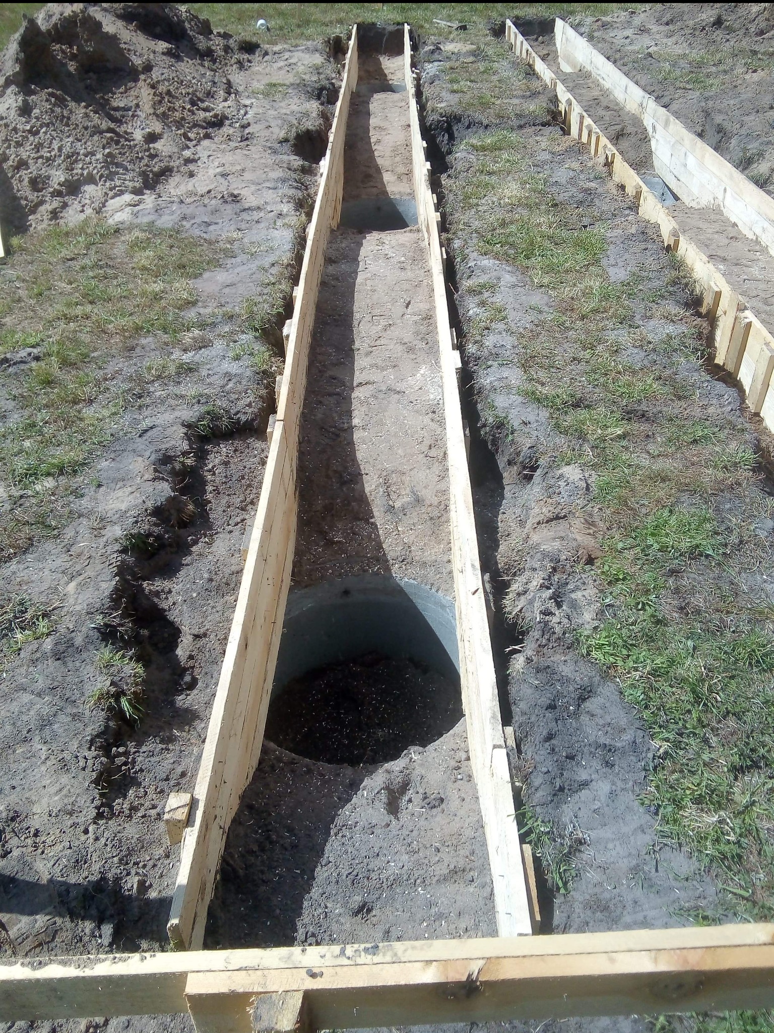 Deskowanie wykopu pod fundamenty, widok z góry. Przygotowanie do wylania betonu, ziemia z fragmentami trawy. Prace ziemne, szalunek z desek.