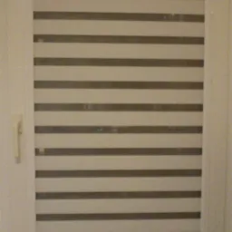 Zamknięta roleta w biało-szare pasy w oknie z białym obramowaniem, widoczna klamka okienna.