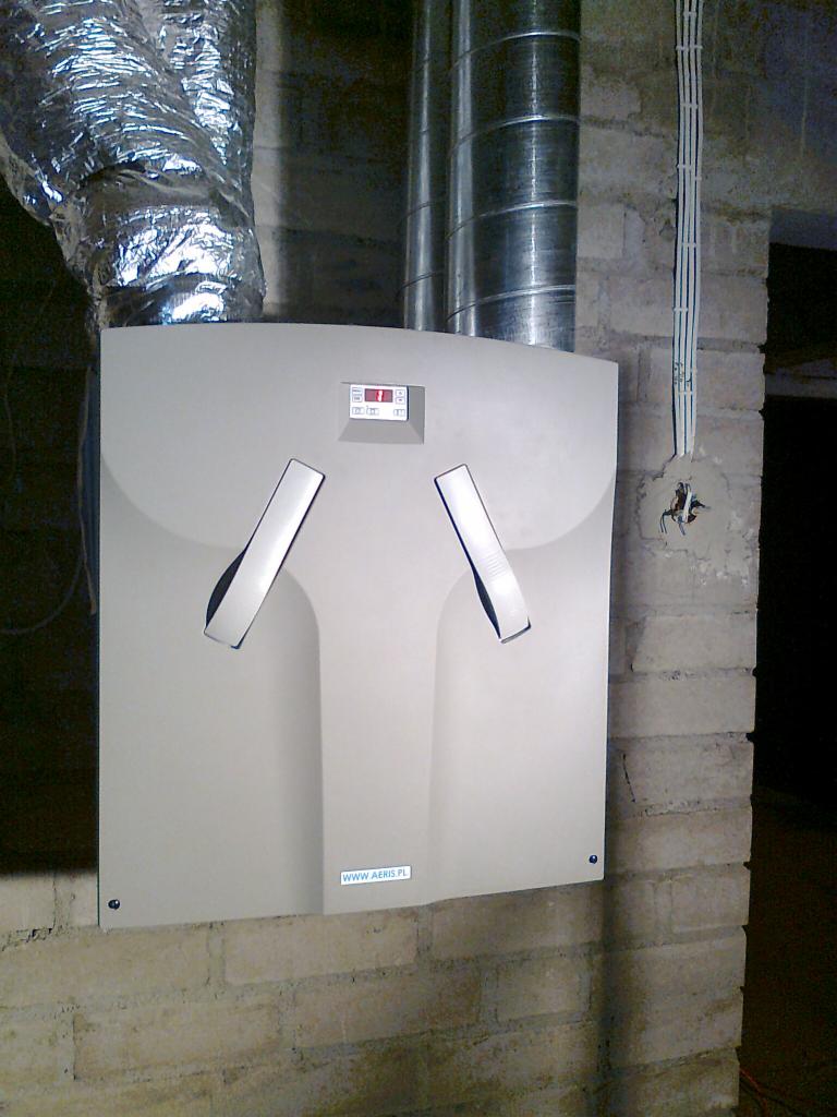 Zamontowany centralny rekuperator z dwoma anemostatami na ścianie z cegły. Widoczne przewody wentylacyjne i instalacja elektryczna. Aeris.pl