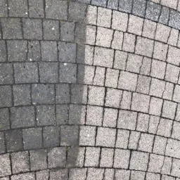Częściowo wyczyszczona, szara kostka brukowa, widoczna różnica w kolorze i czystości między czyszczoną a nieczyszczoną powierzchnią.