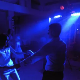 Para tańczy w niebieskim świetle reflektorów podczas imprezy, widoczny sprzęt nagłośnieniowy i oświetleniowy