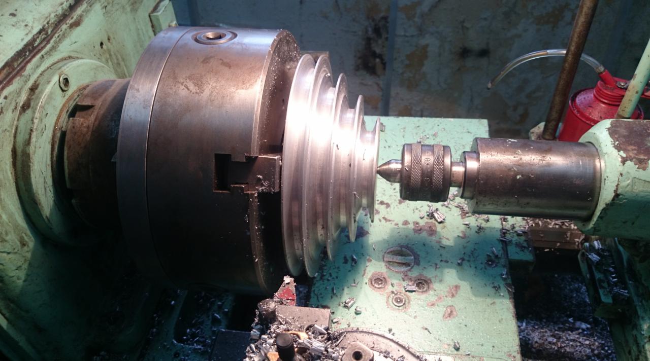 Metalowa część obrabiana na tokarce, wióry na stole, widoczny uchwyt tokarski i narzędzie tnące. Obróbka skrawaniem na maszynie w warsztacie.