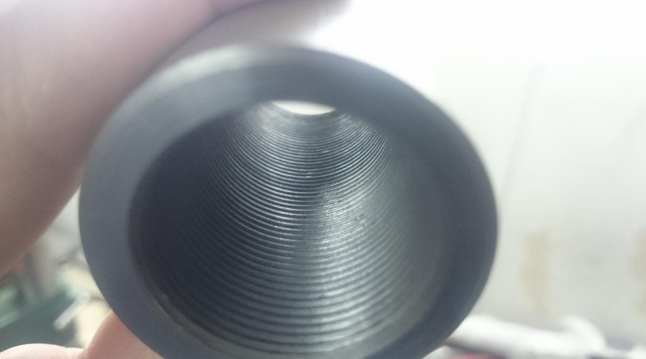 Wnętrze metalowej tulei z precyzyjnie wykonanym gwintem, trzymanej w dłoni. Widok z perspektywy otworu, ukazujący regularne rowki i gładką powierzchnię metalu.