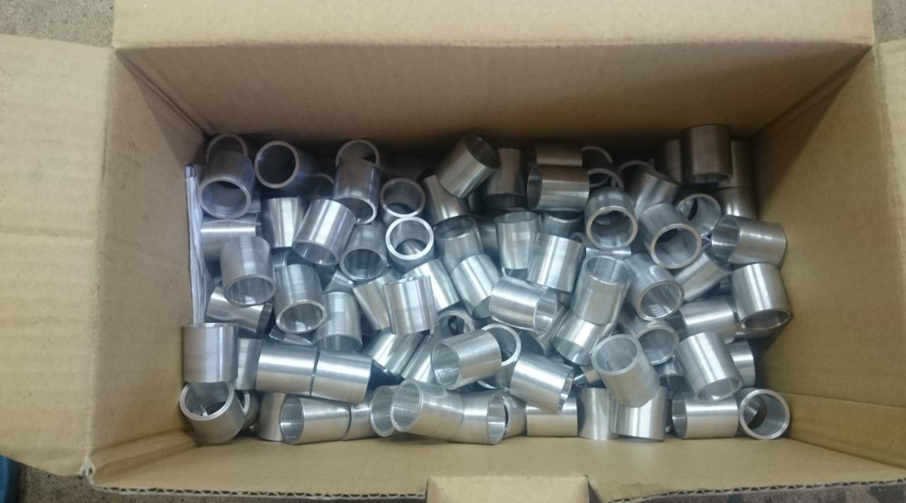 Karton wypełniony dużą ilością metalowych tulejek, prawdopodobnie po obróbce, ułożonych chaotycznie. Widoczne ślady po procesie produkcyjnym.