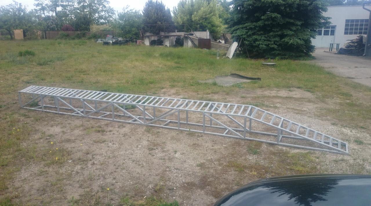 Metalowa konstrukcja rampy na trawiastym terenie, spawana z profili, widoczna część samochodu, zieleń w tle. Gotowy element konstrukcyjny na zewnątrz.
