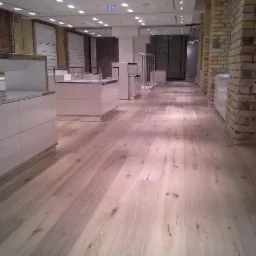 Jasna, drewniana podłoga w sklepie z surową cegłą na ścianach i białymi meblami ekspozycyjnymi.