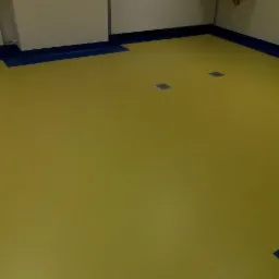 Żółta podłoga z dwoma metalowymi wpuszczanymi puszkami elektrycznymi, wykończona niebieską listwą przypodłogową.