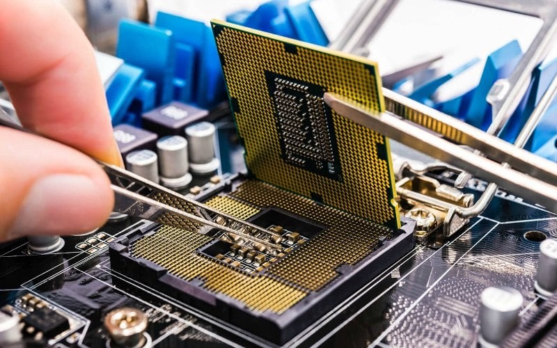 Instalacja procesora CPU w gnieździe płyty głównej za pomocą pęsety, widoczne elementy płyty głównej i radiator chłodzenia.