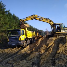 Usługi Sprzętowo Budowlane Ewa Źurawińska - Żółty koparka CAT 318B nabiera urobek do ciężarówki SCANIA P380 na tle lasu i błękitnego nieba. Widoczne ślady opon na ziemi.