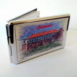 Otwarty, metalowy wizytownik z nadrukiem rysunku zamku w Sandomierzu, widoczne białe wizytówki w środku, na białym tle.