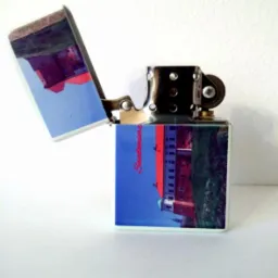 Otwarta zapalniczka z nadrukiem kolorowego zdjęcia Zamku Królewskiego w Sandomierzu, na białym tle. Widoczny mechanizm zapalniczki.