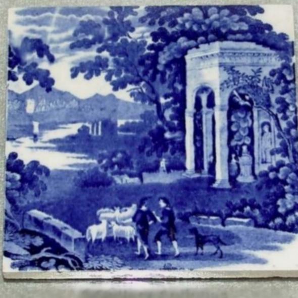 Dekoracyjna płytka ceramiczna w odcieniach błękitu, przedstawiająca sielankowy krajobraz z pasterzami, owcami i architekturą klasycystyczną. Delikatne detale.