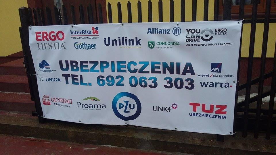 Baner reklamowy z logotypami różnych firm ubezpieczeniowych, numerem telefonu i hasłem 'Ubezpieczenia'. Widoczny na zewnątrz, przymocowany do ogrodzenia.