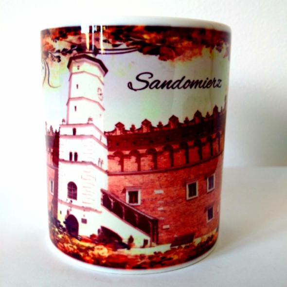 Kubek z nadrukiem wieży ratuszowej i fragmentu murów obronnych Sandomierza. Całość w jesiennej kolorystyce, z napisem 'Sandomierz'.