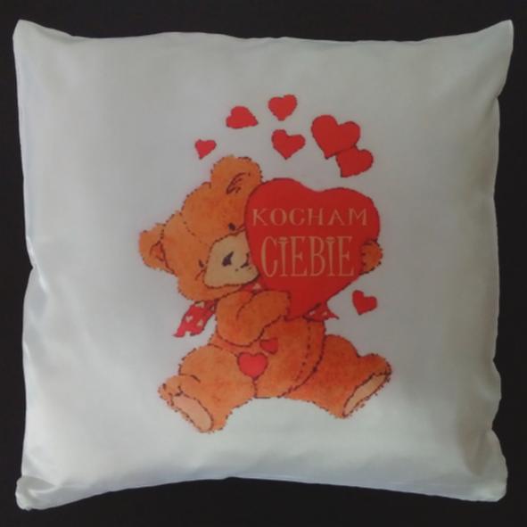 Biała poduszka z nadrukiem pluszowego misia trzymającego serce z napisem 'Kocham Cię', otoczonego czerwonymi sercami. Romantyczny prezent.