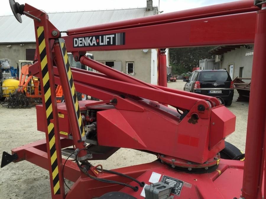 Czerwony podnośnik elektryczny DENKA LIFT DL 15 z widocznym logo, zaparkowany na zewnątrz, w tle budynek i samochód.