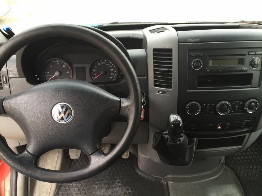 Wnętrze kabiny pojazdu VW Crafter, widok na deskę rozdzielczą, kierownicę z logo Volkswagen i dźwignię zmiany biegów.