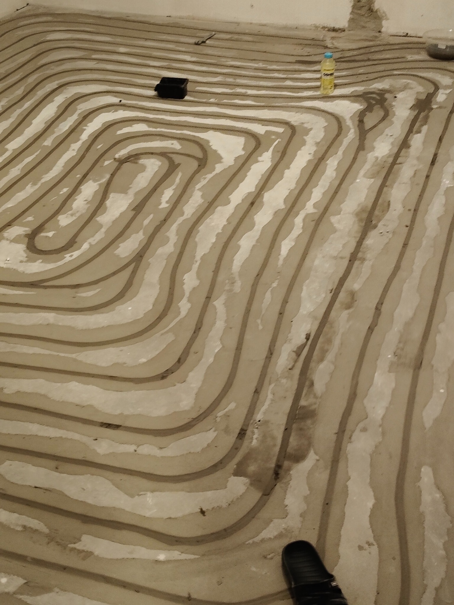 Wykonywanie instalacji w systemie pętli meandrycznej, rury w warstwie wylewki, widoczna butelka z płynem i czarny pojemnik.