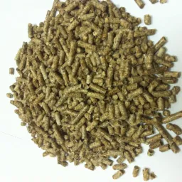 Kupa brązowego pelletu drzewnego na białym tle, z widoczną strukturą włókien drzewnych i nieregularnym kształtem granulek. Widok z góry, lekko z boku.