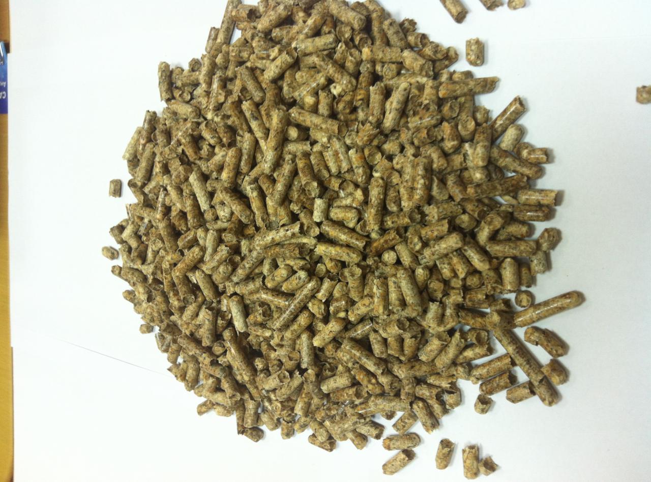 Kupa brązowego pelletu drzewnego na białym tle, z widoczną strukturą włókien drzewnych i nieregularnym kształtem granulek. Widok z góry, lekko z boku.