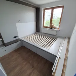 Montaż ramy ł&oacute;żka z szufladami i zabudową wnęki w pokoju w Krakowie, widoczne listwy przypodłogowe do zamontowania.