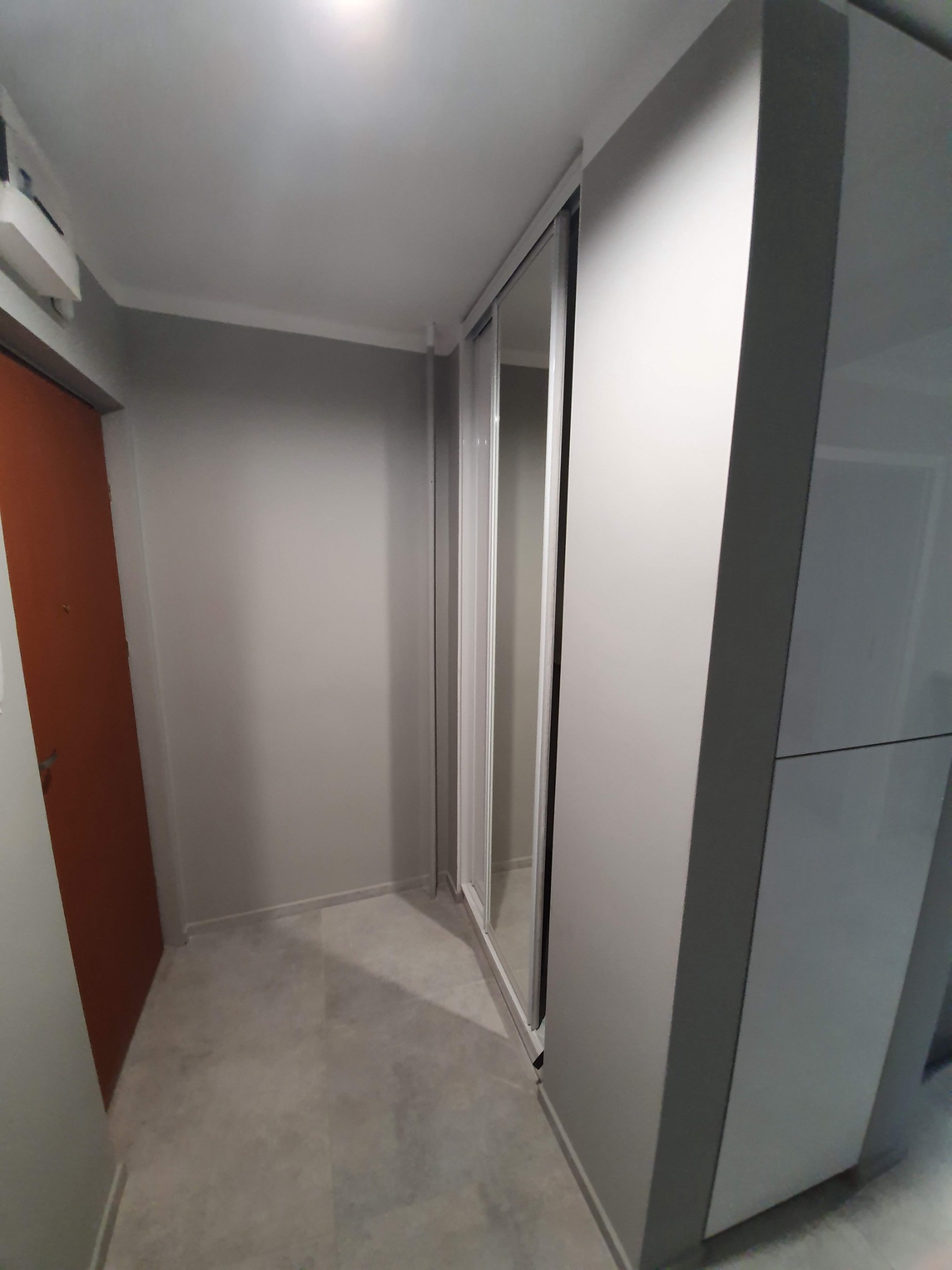 Przedpokój z szarą ścianą, brązowymi drzwiami i szafą wnękową z przesuwnymi lustrzanymi drzwiami, widok z dołu.