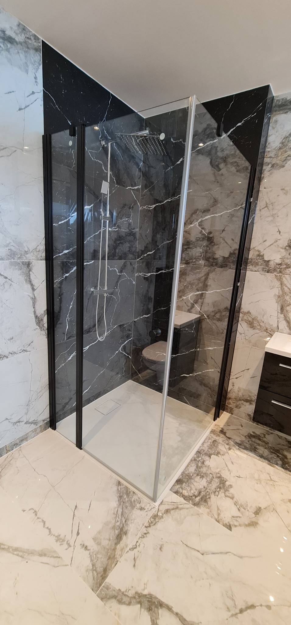 Nowoczesna kabina prysznicowa z deszczownicą, czarne ramy i marmurowe płytki w łazience z jasną podłogą.