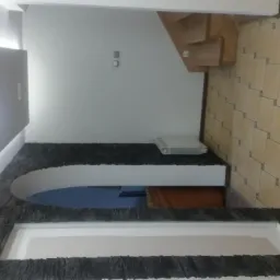 Aranżacja wnętrza z dekoracyjnym łukiem obłożonym czarnym kamieniem, białe ściany, beżowa podłoga z płytek, widoczny fragment schodów i grzejnik na ścianie.