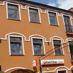 Odnowiona elewacja budynku w odcieniach pomarańczy z białymi zdobieniami okien i gzymsów, widoczne rusztowania i szyld Banku Pekao.