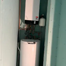 Nowy, biały piec gazowy Viessmann zamontowany w pomieszczeniu z surowymi ścianami z płyt gipsowo-kartonowych, widoczne miedziane rury instalacji grzewczej.