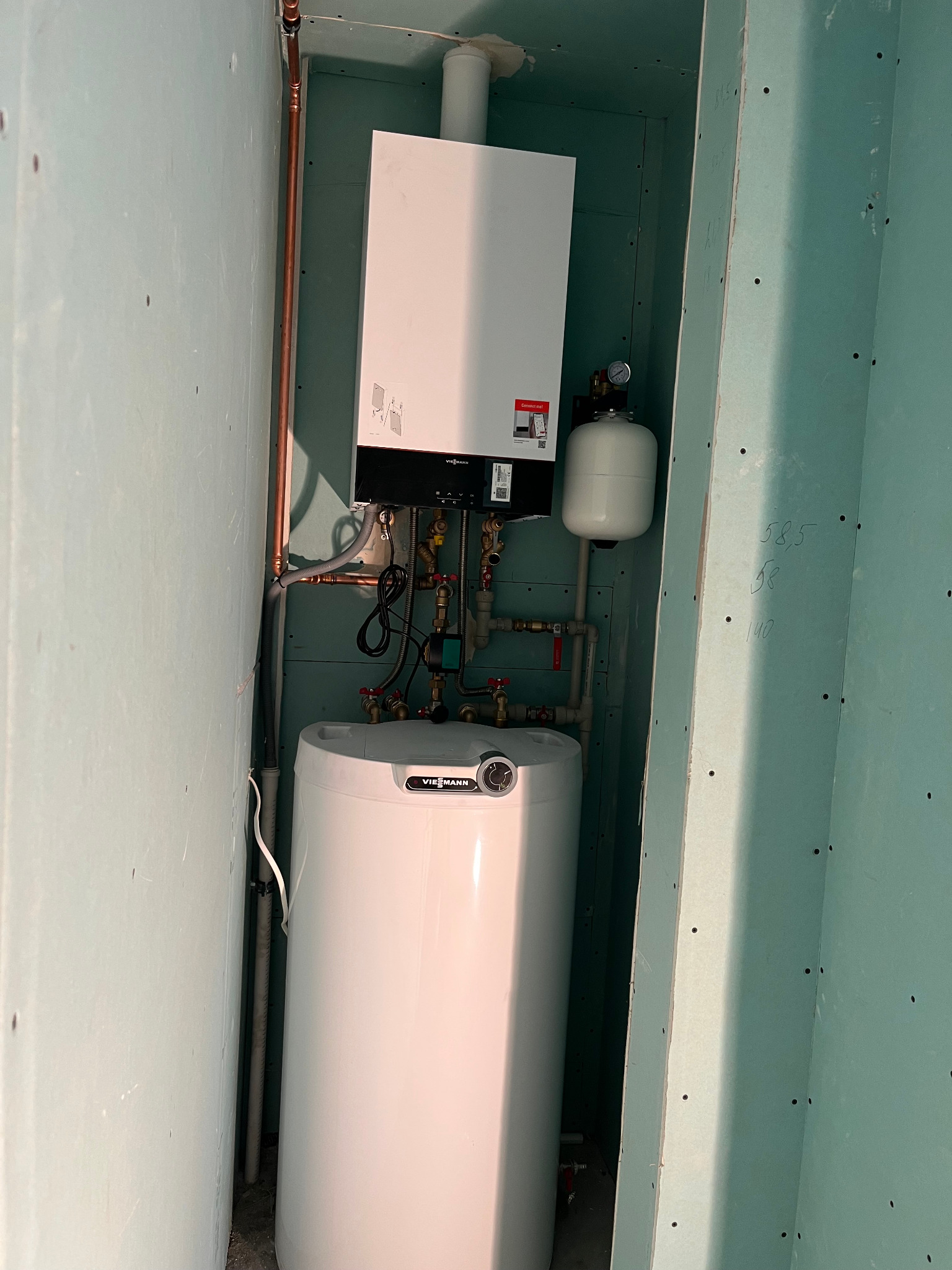 Nowy, biały piec gazowy Viessmann zamontowany w pomieszczeniu z surowymi ścianami z płyt gipsowo-kartonowych, widoczne miedziane rury instalacji grzewczej.