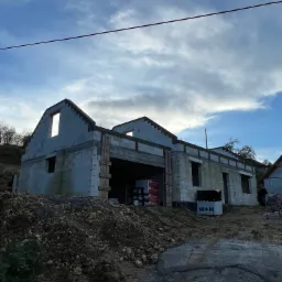 Surowy stan budowy domu z bloczków, widoczne pakiety bloczków H+H, ziemia i niebo z chmurami w tle.