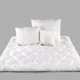 Biała, pikowana kołdra i poduszki z delikatnym wzorem na szarym tle. Widoczne metki na poduszkach. Zestaw pościeli w neutralnej kolorystyce.