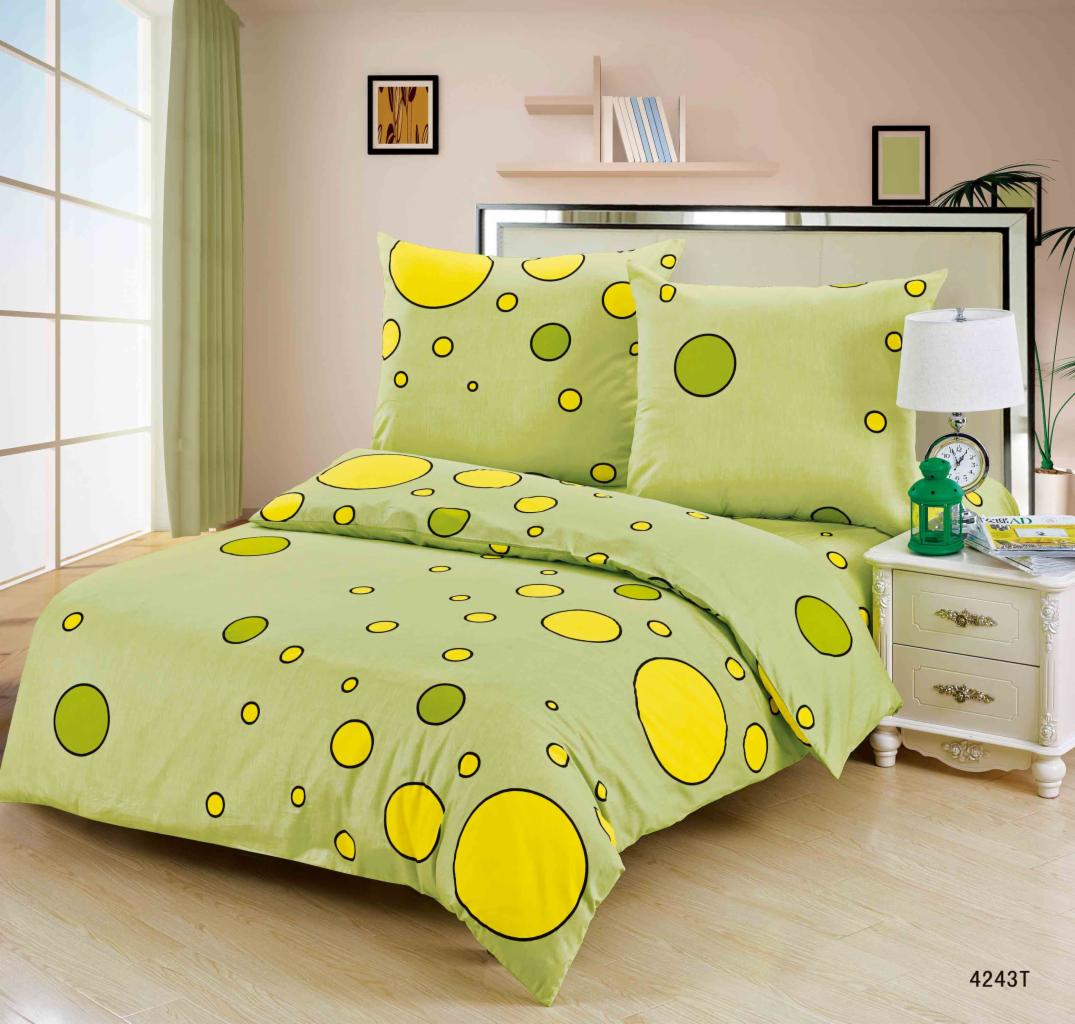 Komplet pościeli w odcieniach zieleni z żółtymi i zielonymi okręgami na łóżku z białą szafką nocną i lampką. Duże okno w tle.