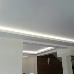 Nowoczesny sufit podwieszany z oświetleniem LED w jasnym pomieszczeniu. Widoczne elementy dekoracyjne i staranne wykończenie.