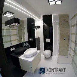 Nowoczesna łazienka z czarno-białymi akcentami, owalną umywalką nablatową, podwieszaną toaletą i kabiną prysznicową z poziomymi pasami, oświetleniem LED pod lustrem i geometryczną lampą sufitową.