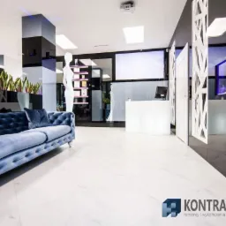 Eleganckie wnętrze biurowe z marmurową posadzką, błękitną sofą Chesterfield i recepcją z podświetleniem LED, akcentowane roślinami w donicach i akwarium z rybami.