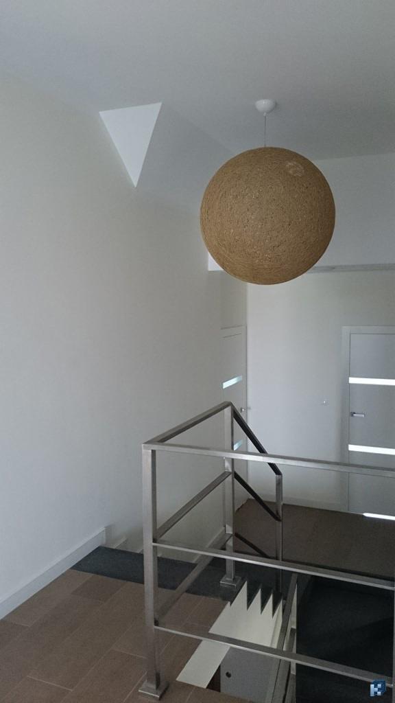 Nowoczesne wnętrze z oświetleniem kulistym i metalową balustradą schodów. Minimalistyczny design z geometryczną dekoracją ścienną.