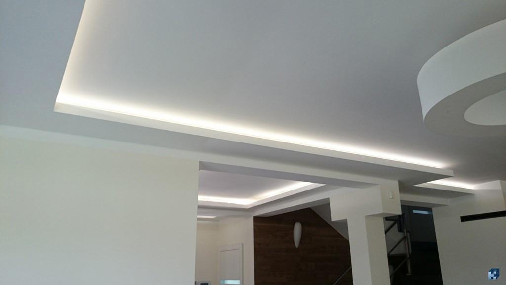 Nowoczesny sufit podwieszany z oświetleniem LED w jasnym pomieszczeniu. Widoczne elementy dekoracyjne i staranne wykończenie.