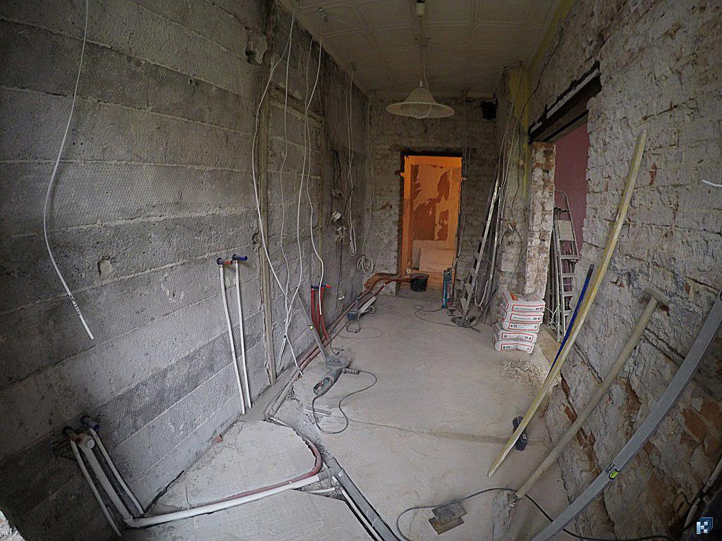 Wnętrze w trakcie remontu we Wrocławiu: odsłonięte cegły, instalacje, worki z zaprawą. Widoczne kable i rury, przygotowane do dalszych prac wykończeniowych.