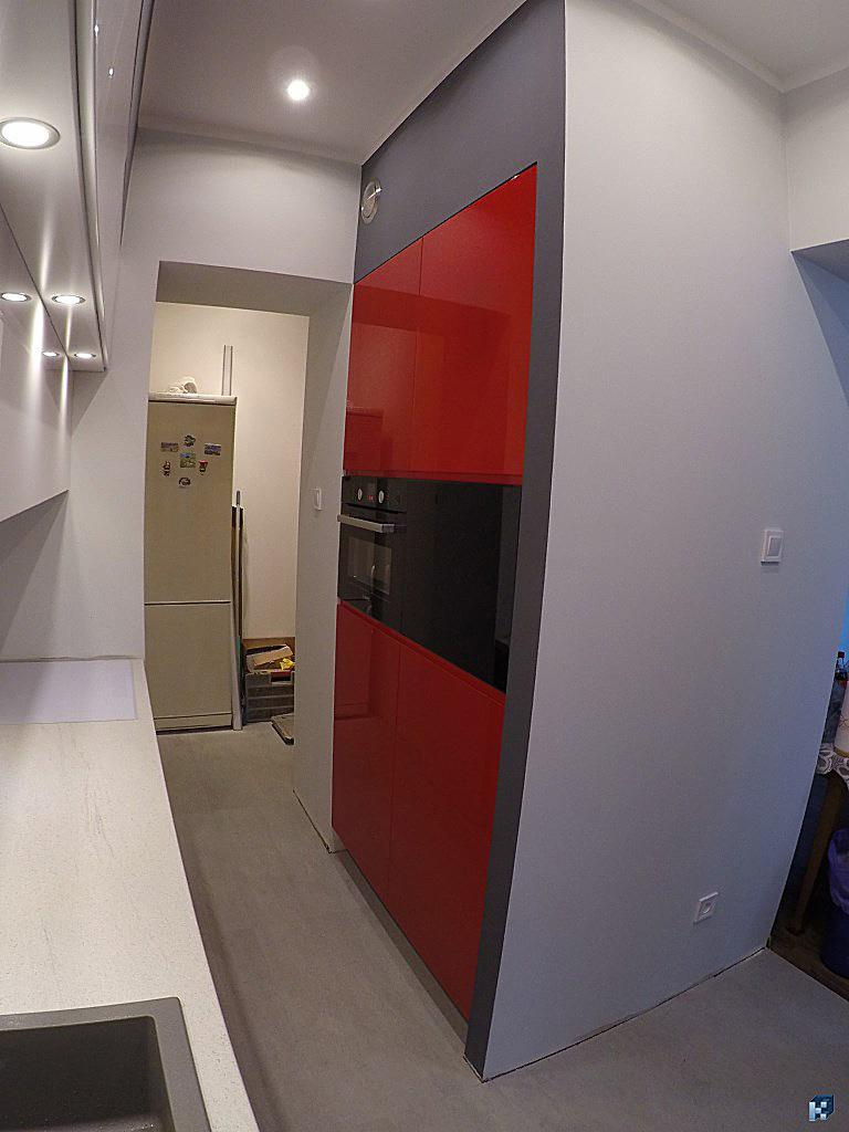 Nowoczesna kuchnia z czerwonymi szafkami i czarnym piekarnikiem w zabudowie, szare ściany i blat, widok z bliska na fragment pomieszczenia.