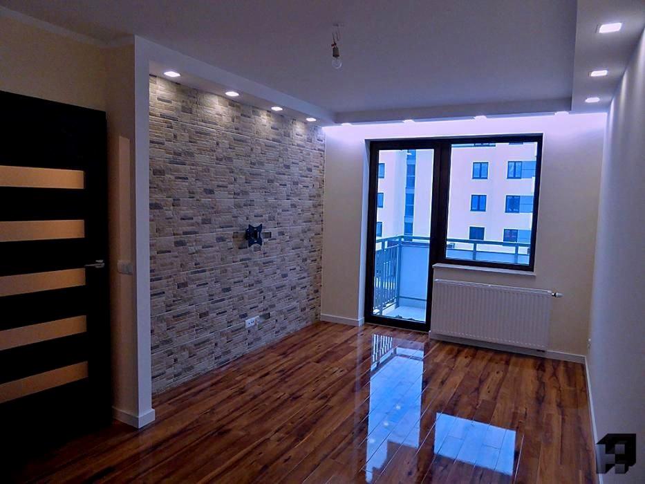 Pokój po remoncie z parkietem o wysokim połysku, ściana akcentowa wyłożona dekoracyjną cegłą, oświetlenie punktowe w suficie i czarne drzwi z poziomymi paskami.