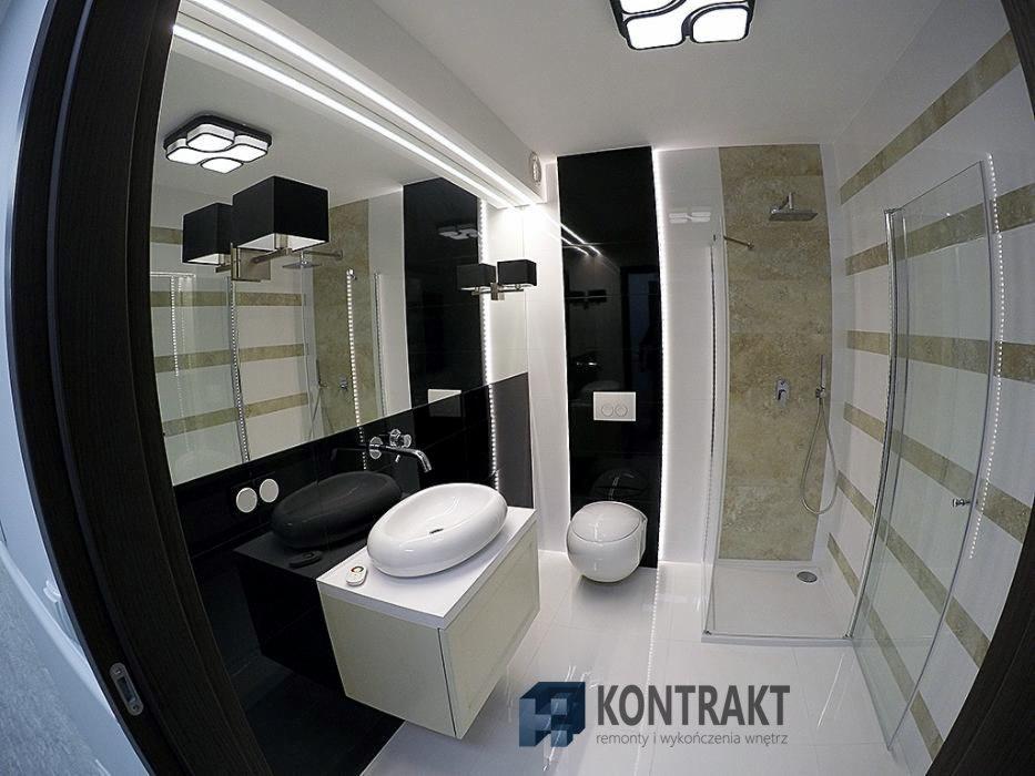 Nowoczesna łazienka z czarno-białymi akcentami, owalną umywalką nablatową, podwieszaną toaletą i kabiną prysznicową z poziomymi pasami, oświetleniem LED pod lustrem i geometryczną lampą sufitową.