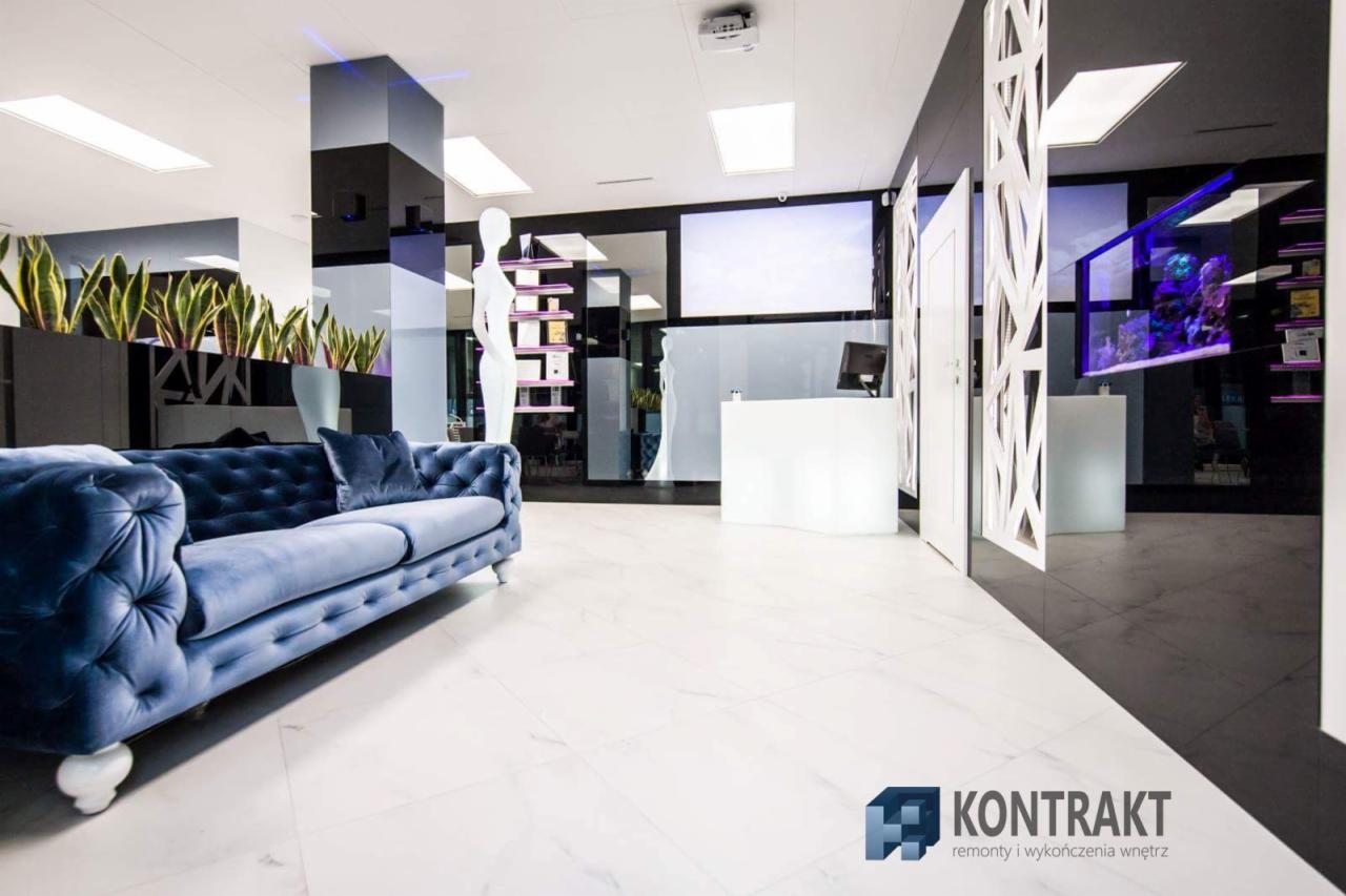 Eleganckie wnętrze biurowe z marmurową posadzką, błękitną sofą Chesterfield i recepcją z podświetleniem LED, akcentowane roślinami w donicach i akwarium z rybami.